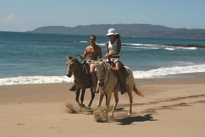 Two riders on horseback along a sandy beach